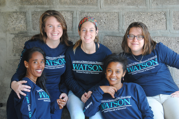Five Watson students smile in front of cement wall