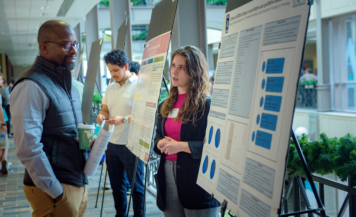 A student explains her research poster to a man attending a student research showcase