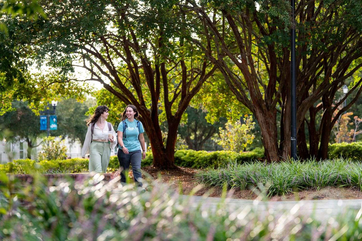 Two students walking on campus sidewalk smiling and talking.