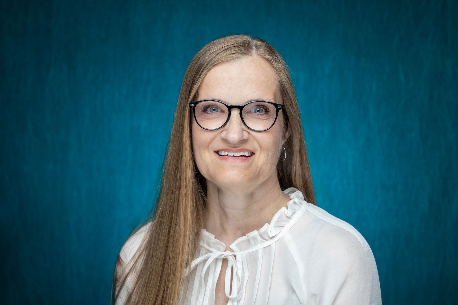 Headshot of woman wearing glasses with teal background