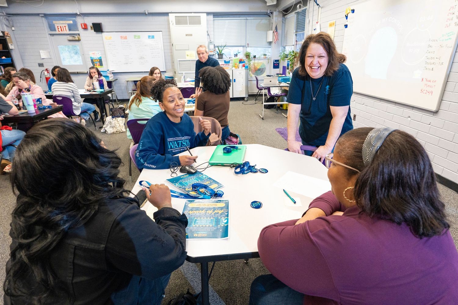Workshop leaders and participating teachers laugh during a workshop in a classroom.