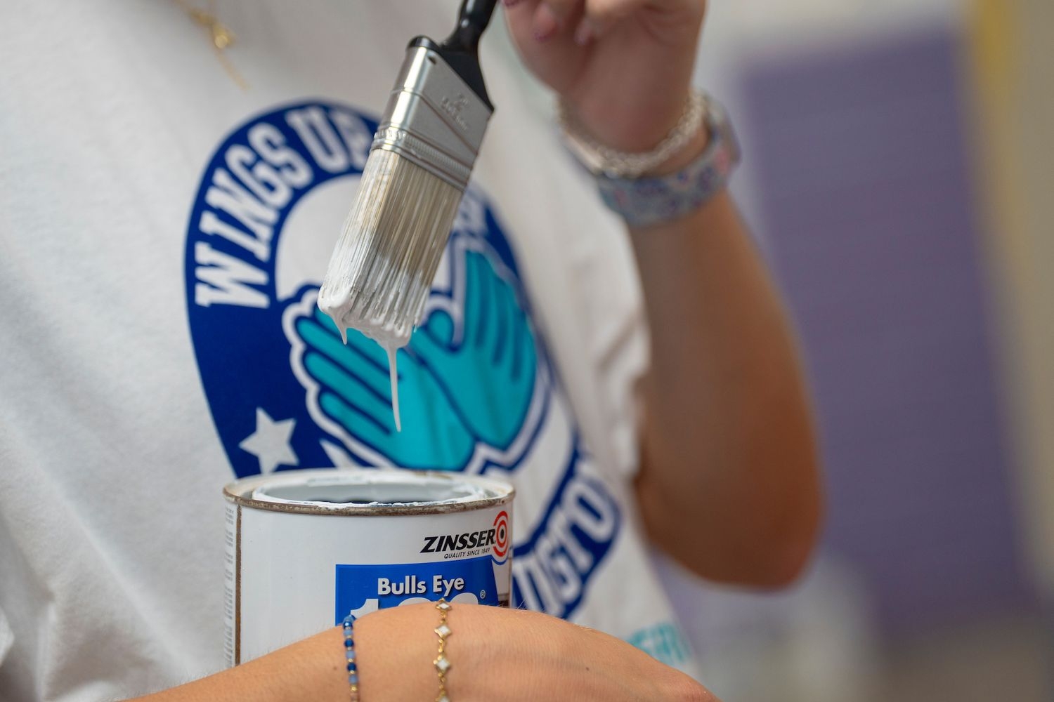 A volunteer holds a can of white paint and paintbrush.