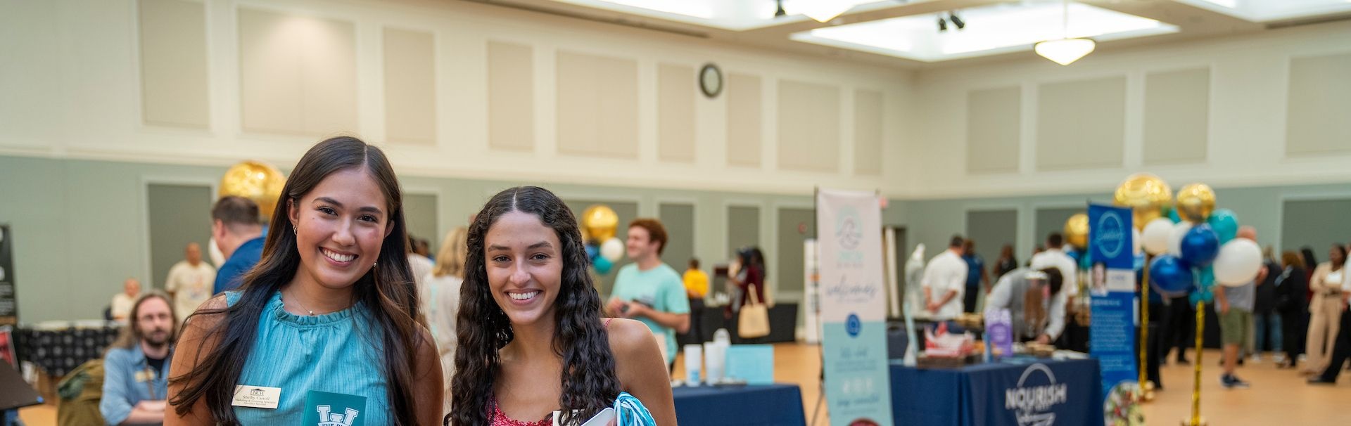 Two attendees stand in front of vendor tables at a UNCW business services fair.