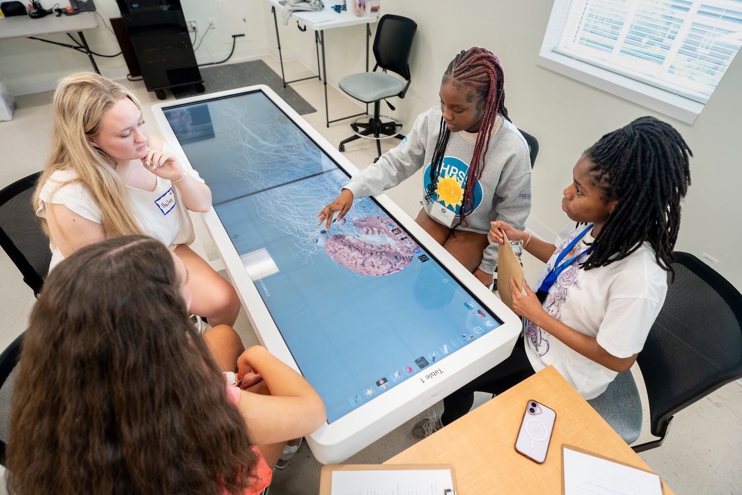 Four iHPSS summer campers sit around an anatomage table to learn about human anatomy. 