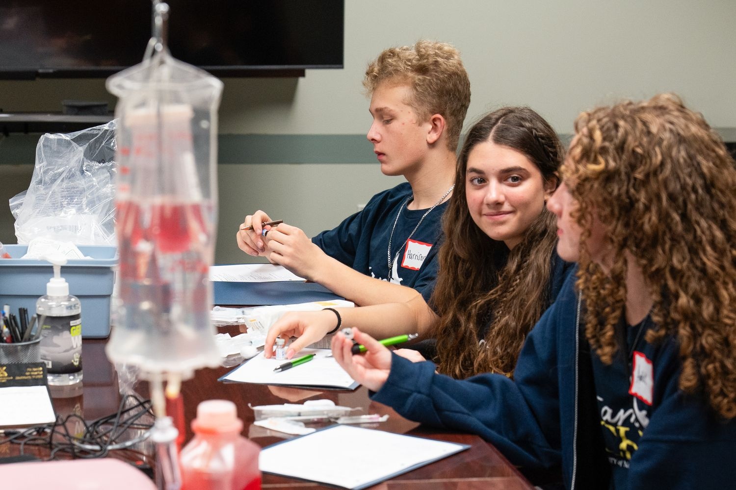 Three iHPSS summer campers examine medical vials while they learn about giving vaccines.