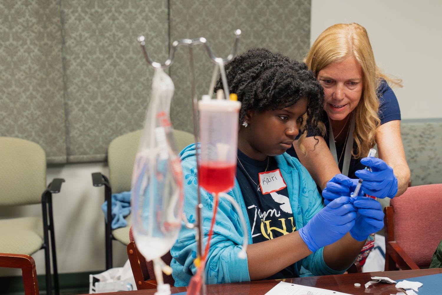 A nurse helps an iHPSS summer camper fill a syringe with liquid from a medical vial to practice giving vaccines.