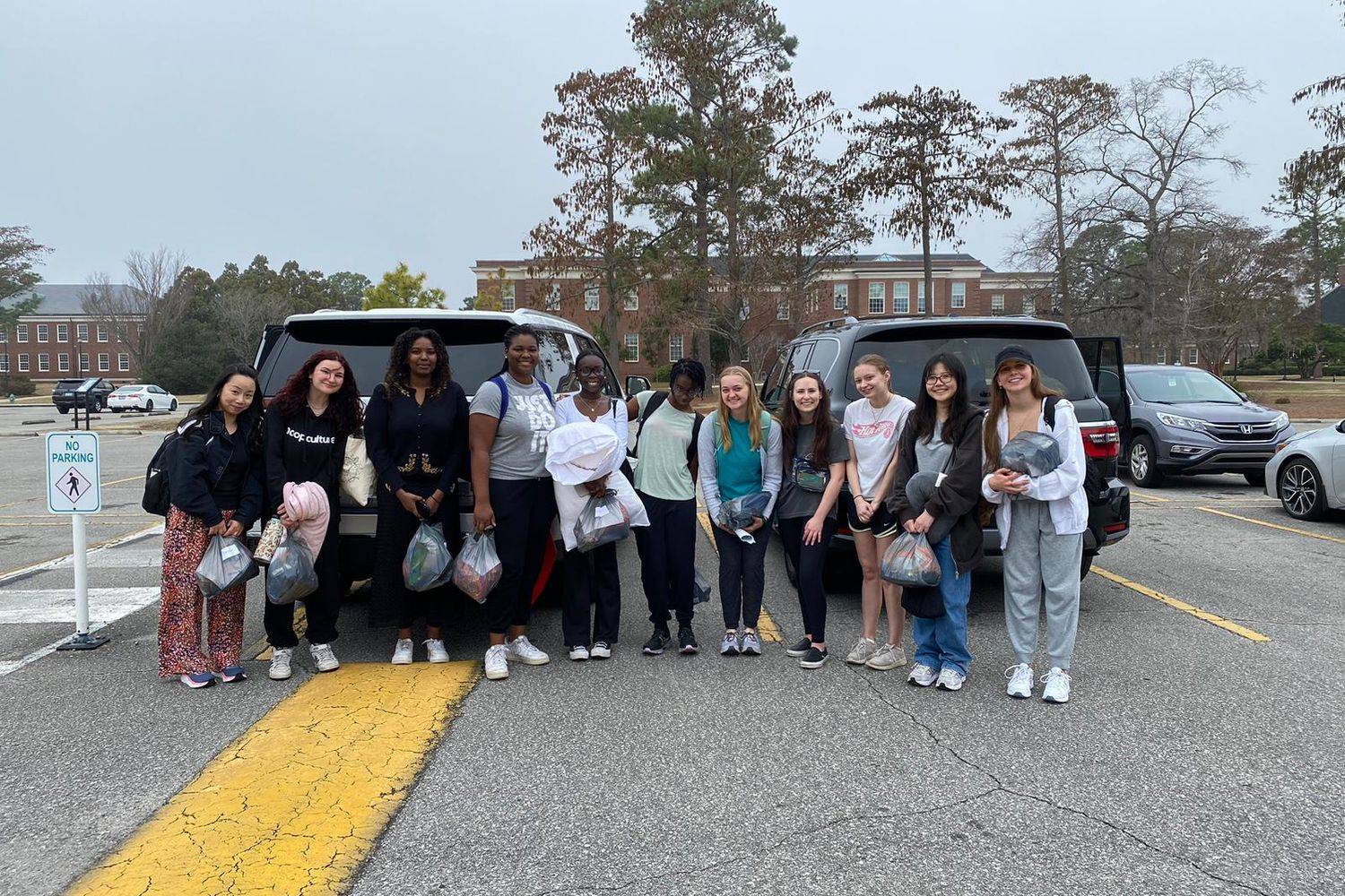 Immersive Service students taking a group photo in front of some cars in a parking lot