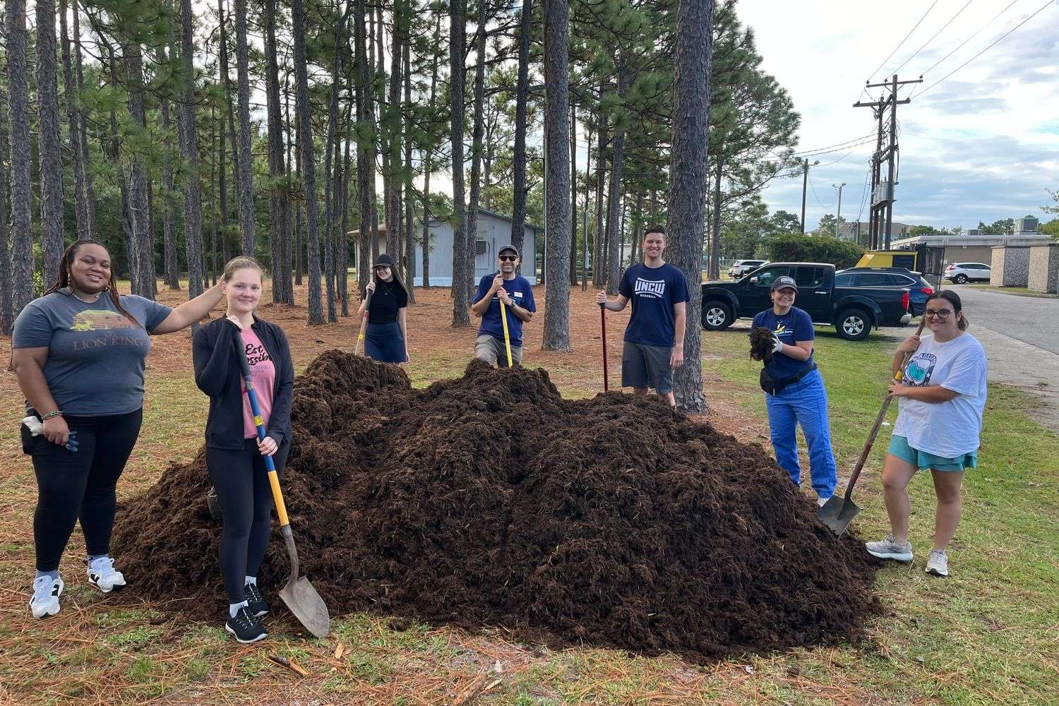 Group of participants circled around a large mound of mulch they're helping spread