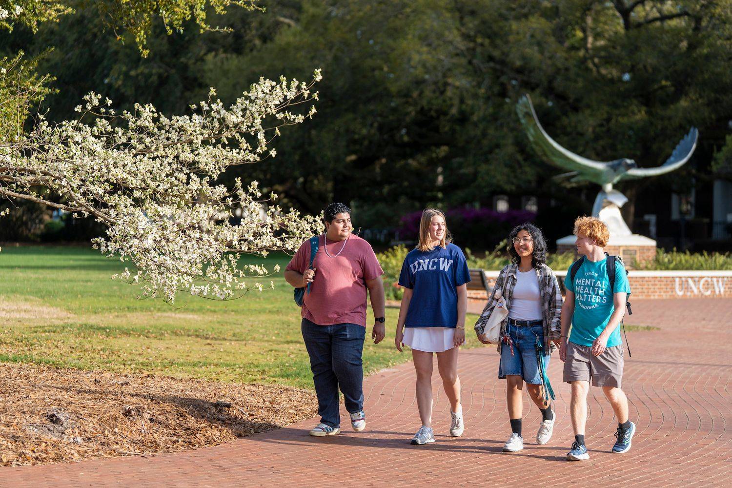 Four students talking in front of a Seahawk statue