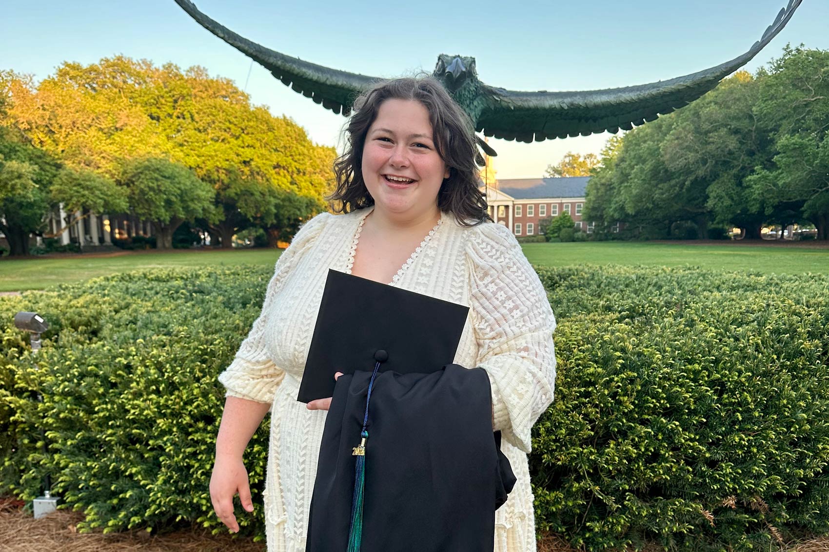 Margarita Bowers Young standing in front of Seahawk statue holding cap and gown
