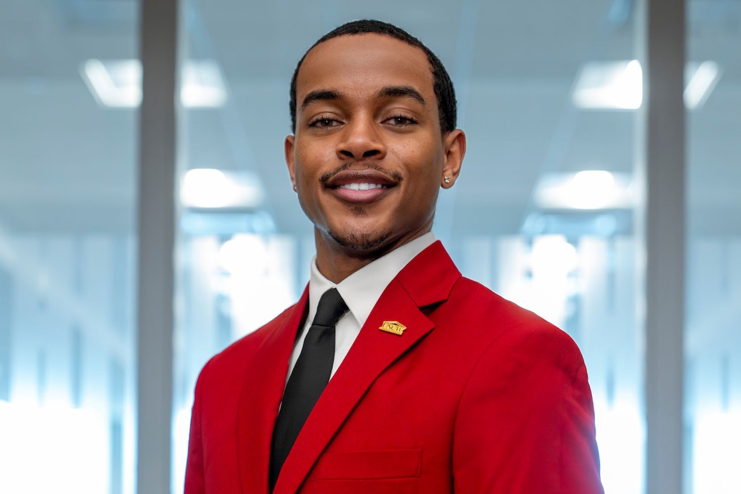UNCW student wearing a red fraternity jacket, posing in a building