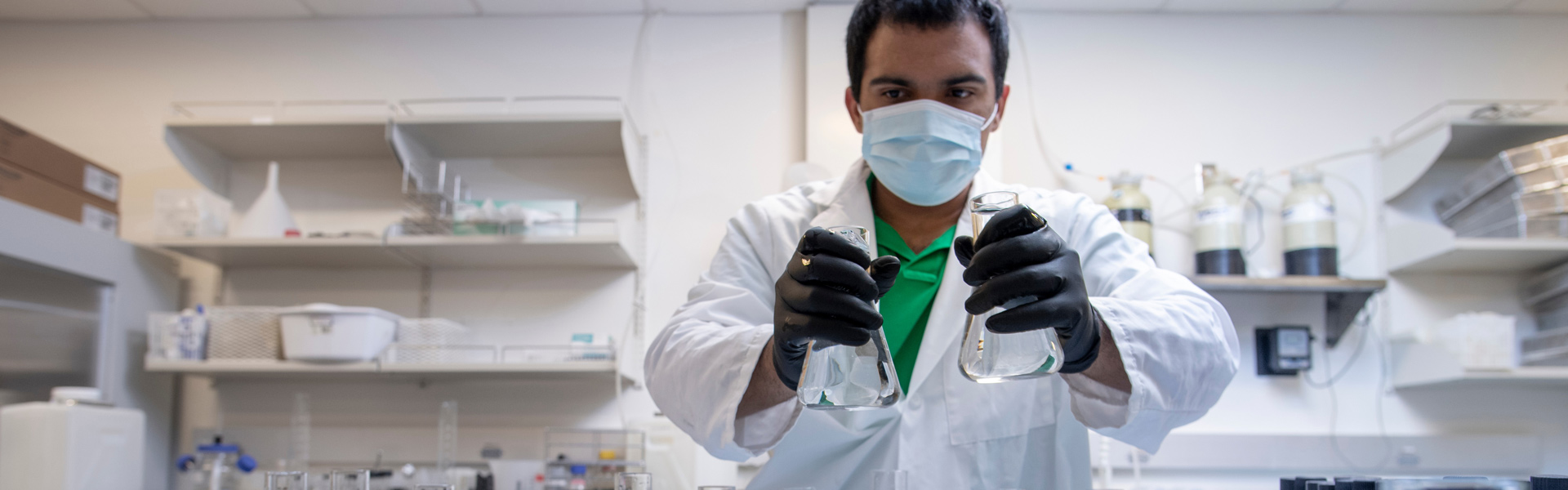 A student in a mask examines two beakers